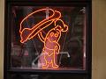 The Frankfurter - neon mascot offering one of his own kind for you to eat